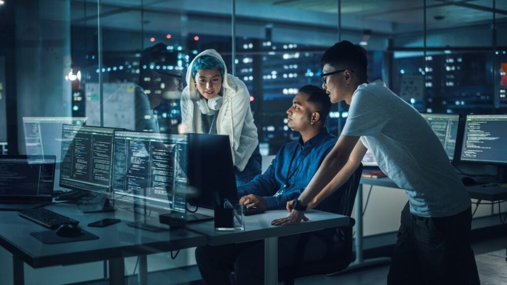 A team of cybersecurity professionals huddle around a computer to discuss strategy.