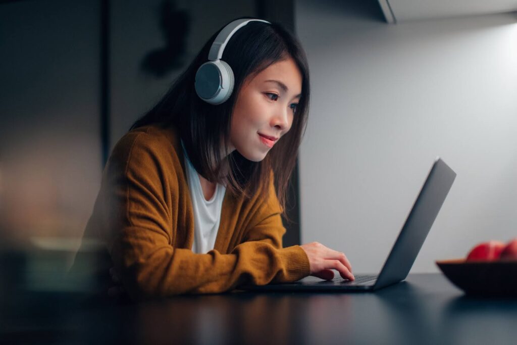 A woman wearing headphones works at a laptop computer.